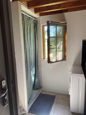A small, enclosed room with a window, a door, and a white appliance, possibly a refrigerator.