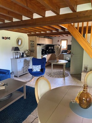A cozy living room with a blue armchair, a dining table, and a kitchen in the background.