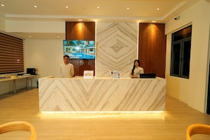 A hotel reception desk with a marble design, a television displaying a resort, and wooden paneling on the walls. - Cocotree Resort (Panglao)