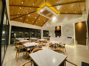 A modern dining area with wooden ceiling beams, marble tables, and chairs. - Cocotree Resort (Panglao)