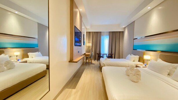 A hotel room with two beds, a TV, a desk, and a view of the outdoors. - Cocotree Resort (Panglao)