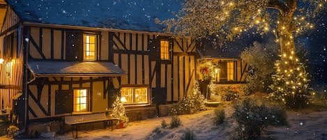 A traditional timber-framed house with a snow-covered yard and illuminated windows.