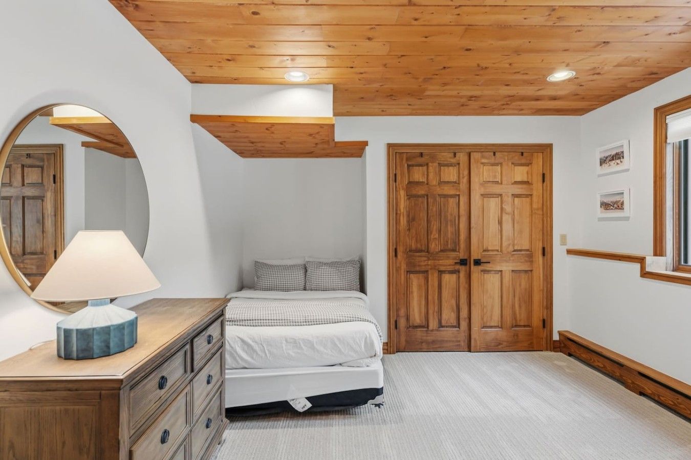 A bedroom with a bed, a dresser, a mirror, and wooden doors.