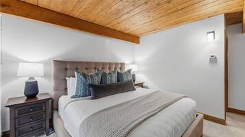 A bedroom with a tufted headboard, a bed with a white comforter, a grey throw blanket, and a nightstand with a lamp.