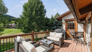 Terraza de madera con mobiliario de mimbre, una parrilla y vista a un campo de golf.