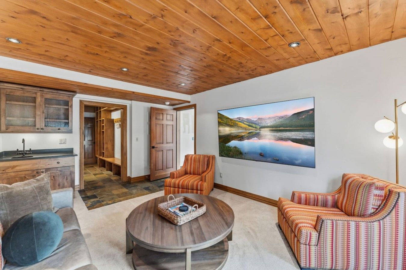 A spacious living area with a wooden ceiling, a large painting of a landscape, and a cozy seating arrangement.