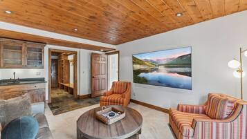 A spacious living area with a wooden ceiling, a large painting of a landscape, and a cozy seating arrangement.