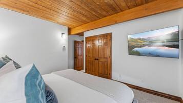 Un dormitorio con una cama, techo de madera, una puerta y un cuadro colgado en la pared.
