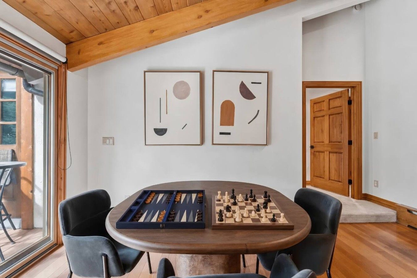 A dining area with a wooden table, two framed abstract artworks, and a chessboard.