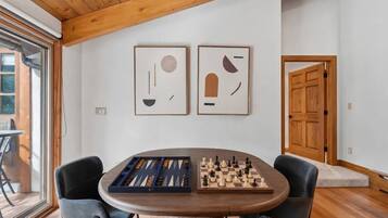 A dining area with a wooden table, two framed abstract artworks, and a chessboard.
