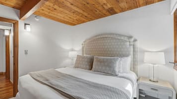 Un dormitorio con techo de madera, una cama con almohadas estampadas, una lámpara de noche y una mesita de noche.