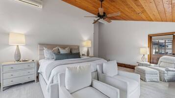 Un dormitorio con cama, mesitas de noche, ventilador de techo y una zona de estar con sillones.