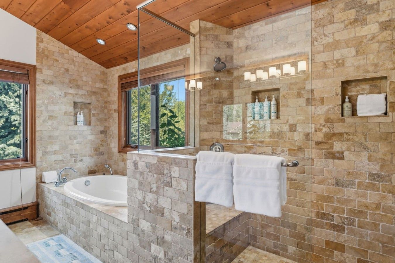 Un baño moderno con una bañera independiente, ducha con cerramiento de vidrio y paredes de piedra.