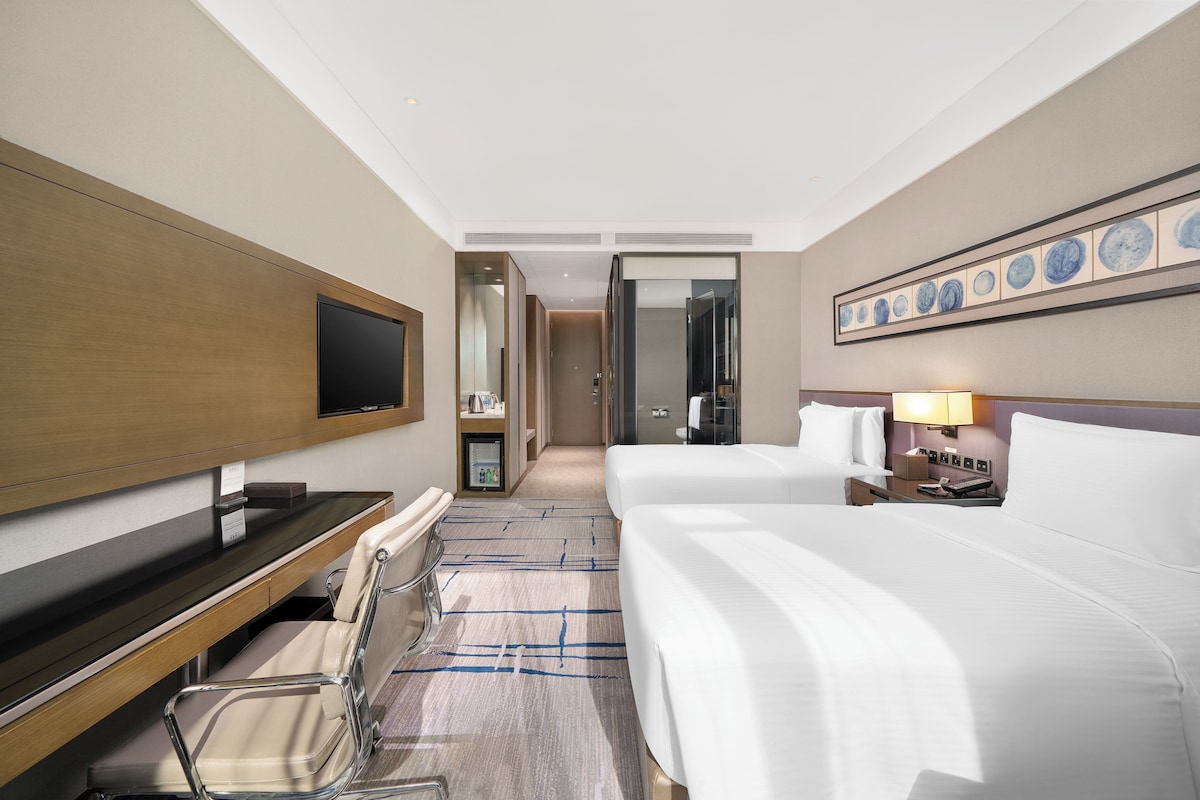 A hotel room with a bed, bedside table, lamp, TV, and a seating area with a chair and a small table.