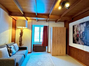 Una stanza accogliente con soffitto in legno, un divano con cuscini, una lampada, un termosifone e un quadro con una veduta cittadina.