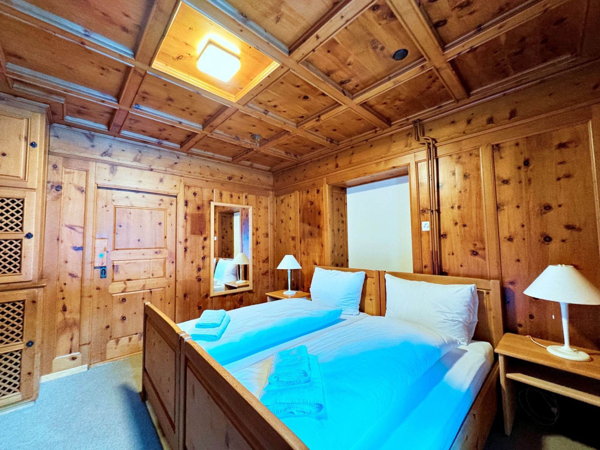 Une chambre dans un chalet en bois, avec un lit, deux tables de chevet, une fenêtre et un luminaire au plafond.