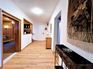 Un corridoio con pavimento in legno, una porta in legno, un piccolo tavolo con una lampada e un arazzo appeso al muro.
