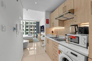 Una cucina moderna con forno integrato, microonde e macchina da caffè. Una grande finestra offre luce naturale e vista dell'esterno dell'edificio.