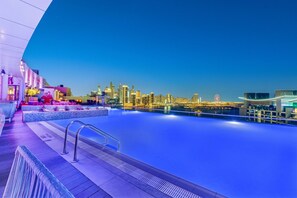 Una piscina sul tetto con vista sullo skyline urbano, un'area relax con una statua di fenicottero rosso e un edificio moderno con facciata curva.