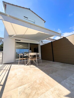 A modern outdoor patio with a table and chairs, a sliding glass door, and a retractable awning. - Sea View · New 2-Room Apt · A/C · Private parking (Vallauris)