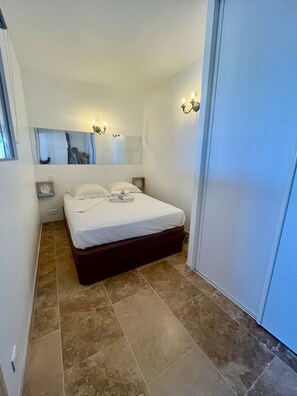 A hotel room with a bed, a nightstand, a mirror, and a wall-mounted light fixture. - Sea View · New 2-Room Apt · A/C · Private parking (Vallauris)