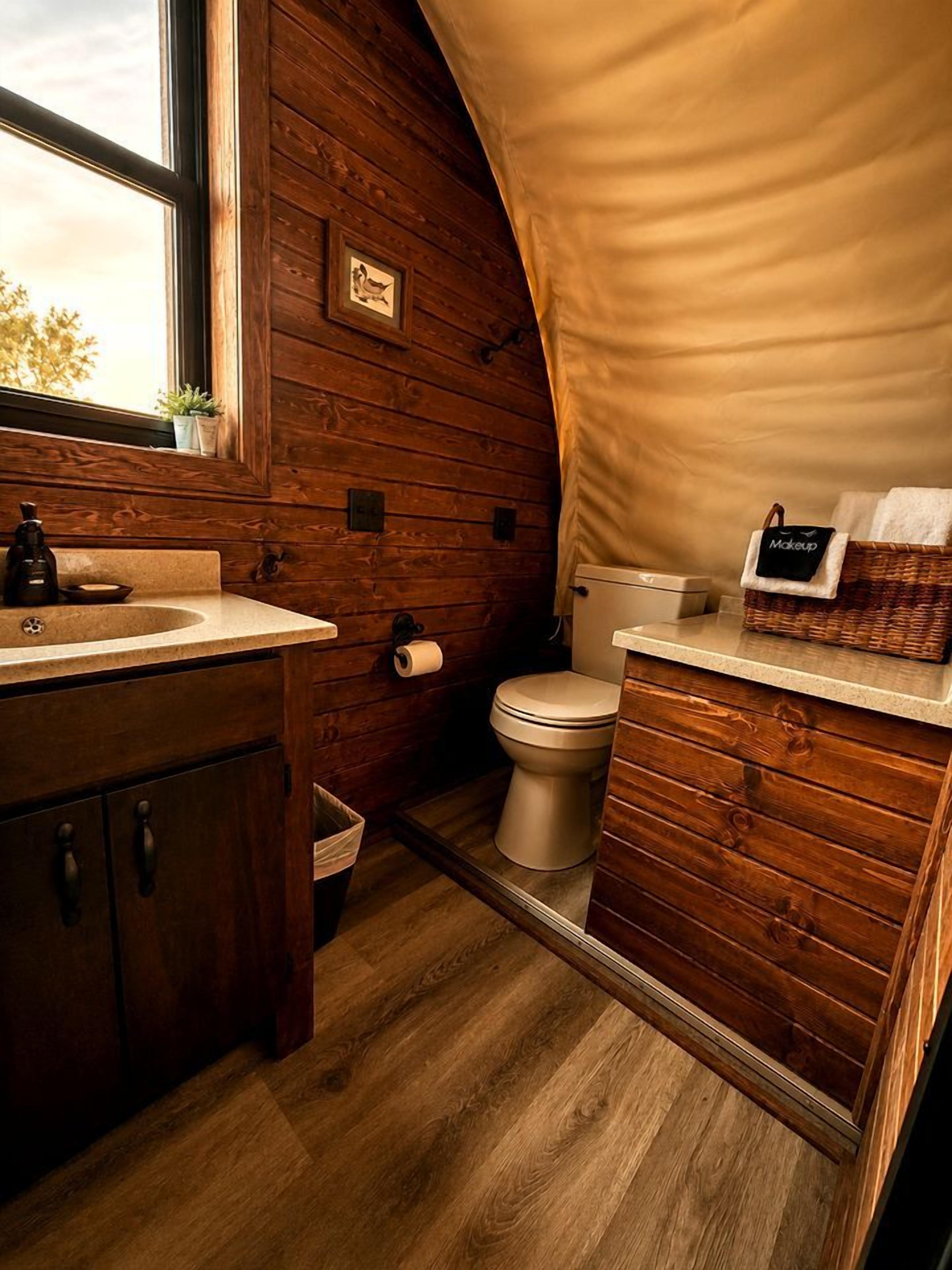 Un baño de madera pequeño y funcional, con lavamanos, inodoro y un ventanal.