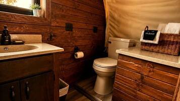 Un baño de madera pequeño y funcional, con lavamanos, inodoro y un ventanal.