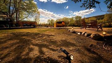 An outdoor area with a dirt ground, wooden chairs, a metal barrel, and a building in the background.