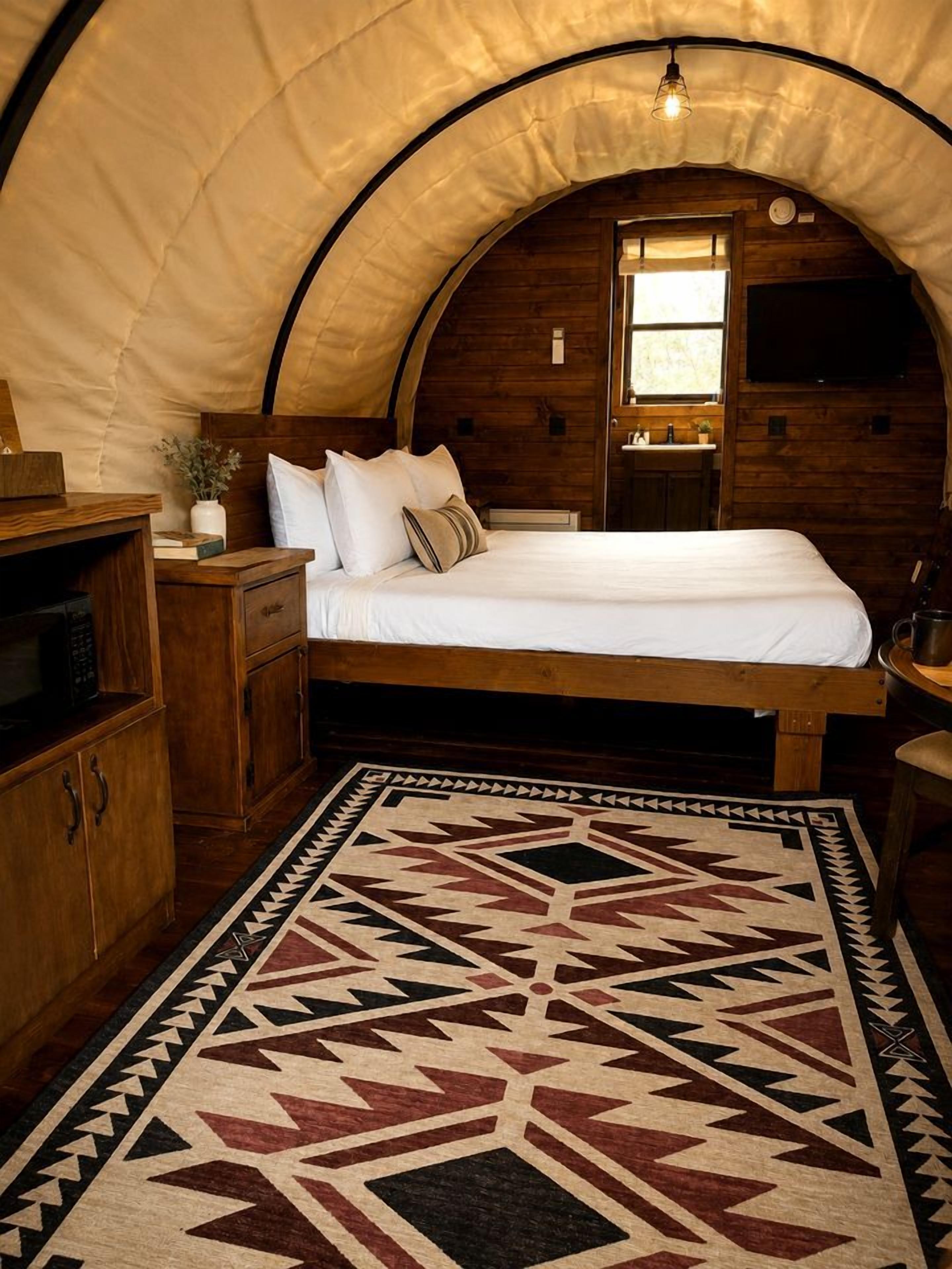 A tent-style bedroom with a bed, wooden furniture, a rug, and a window.