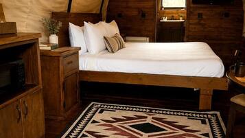 A tent-style bedroom with a bed, wooden furniture, a rug, and a window.