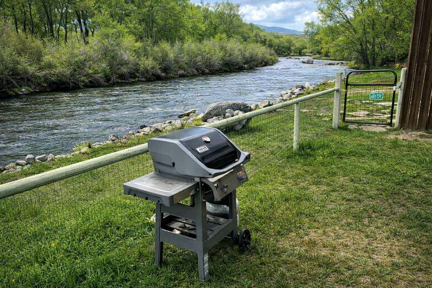 Un juego de parrilla portátil cerca de un río, con una valla y una puerta al fondo.