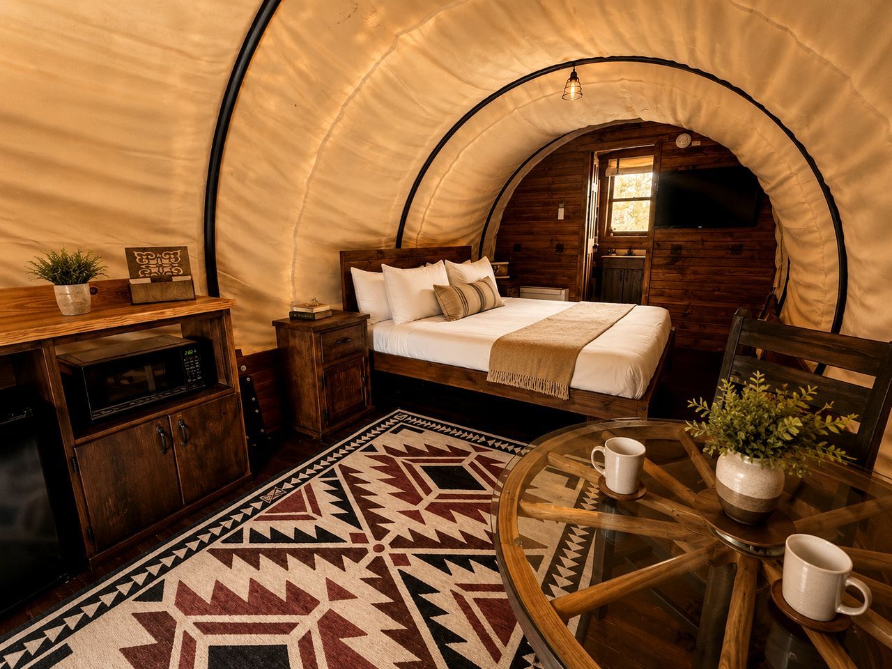 A cozy tent-style room with a bed, a small table with two cups, a cabinet, and a patterned rug.