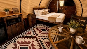 Una camera accogliente in stile tenda, con un letto, un tavolino con due tazze, un armadietto e un tappeto decorato.