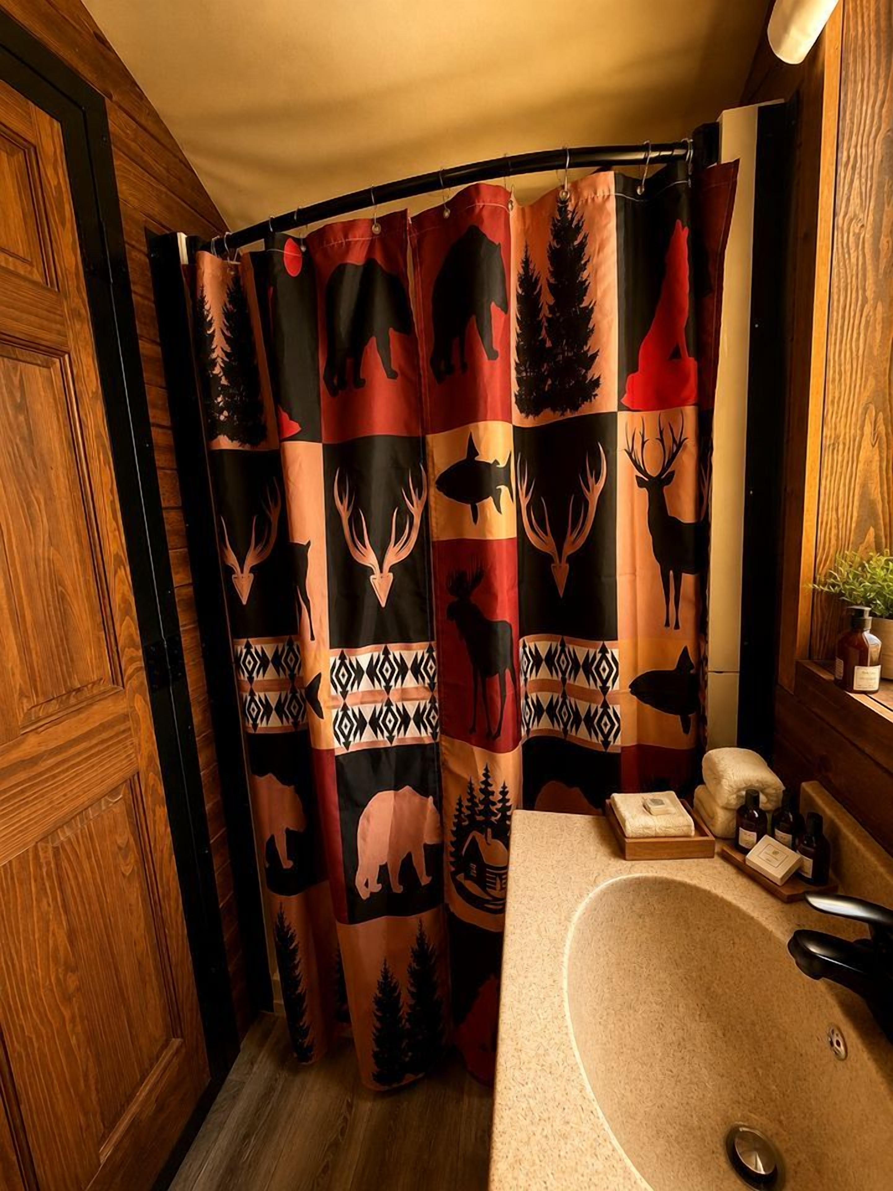 A bathroom with a shower curtain featuring animal prints, a wooden door, and a sink with toiletries.