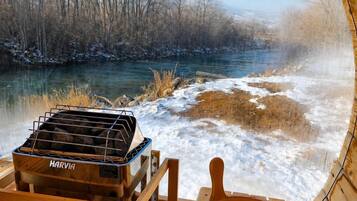 A wooden grill and a wooden bowl on a bench with a view of a river and trees.