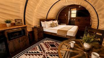 Une pièce confortable aménagée comme une tente, avec un lit, une petite table avec deux tasses, un meuble et un tapis à motifs.