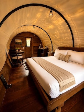 A cozy, arched-roofed bedroom with a wooden bed, a chair, and a small table.
