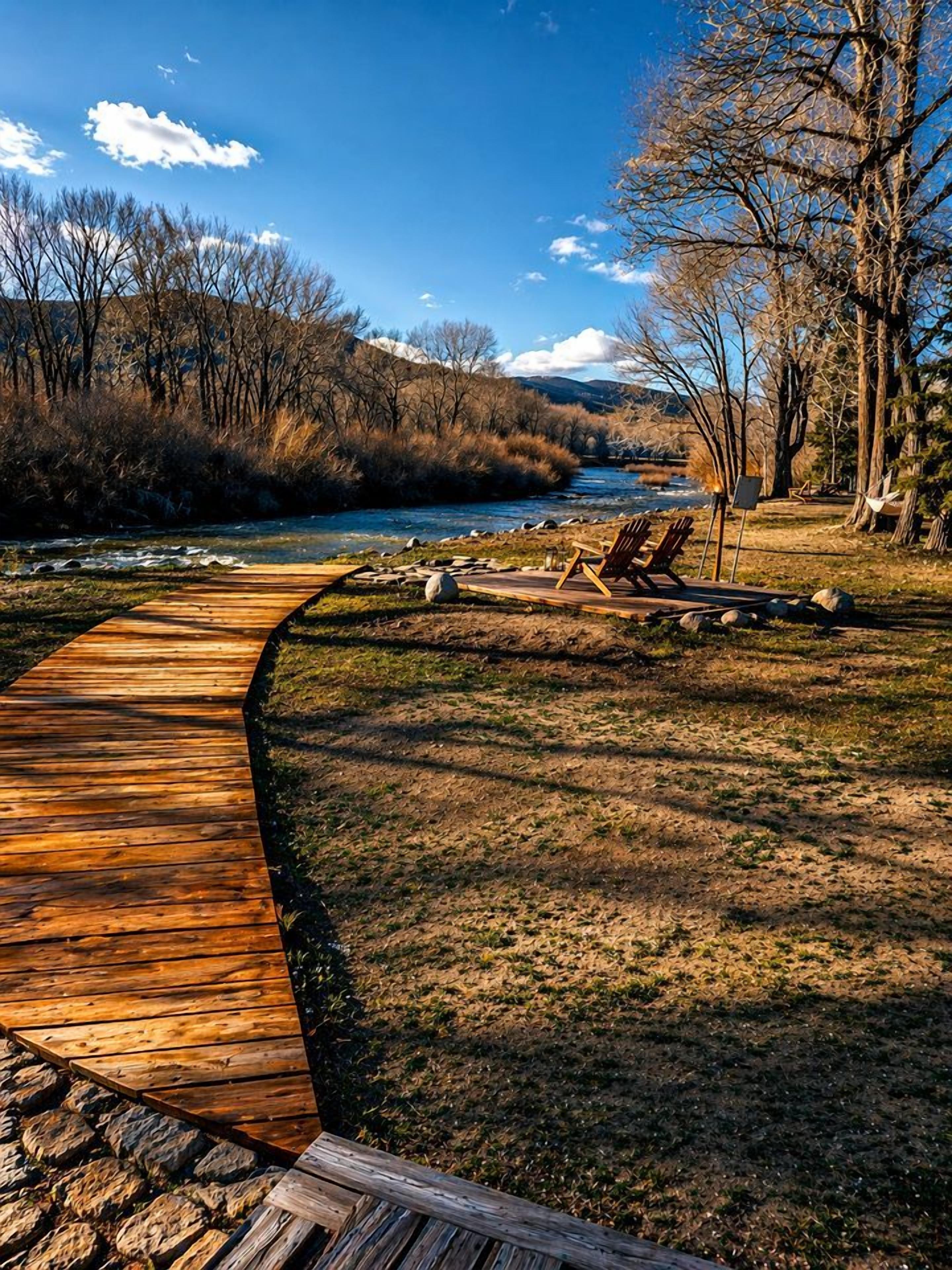 Un camí de fusta que condueix a la riba d'un riu, amb caires i una cadira enfilada.