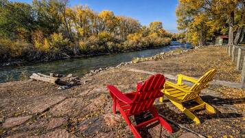 A riverside view with a wooden dock, a red and a yellow chair, and a small cabin in the background.