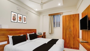 A hotel room with a bed, wooden headboard, a desk with a chair, a wardrobe, a television mounted on the wall, and framed artwork on the wall. - Super Townhouse Marathahalli (Bangalore)