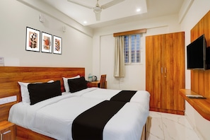 Une chambre d’hôtel comprenant un lit, une tête de lit en bois, un bureau avec une chaise, une armoire, un téléviseur fixé au mur et des œuvres d’art encadrées accrochées au mur.