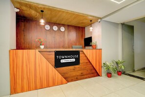 A reception desk with a wooden finish, a clock, a potted plant, and a sign indicating the property is company-serviced. - Super Townhouse Marathahalli (Bangalore)