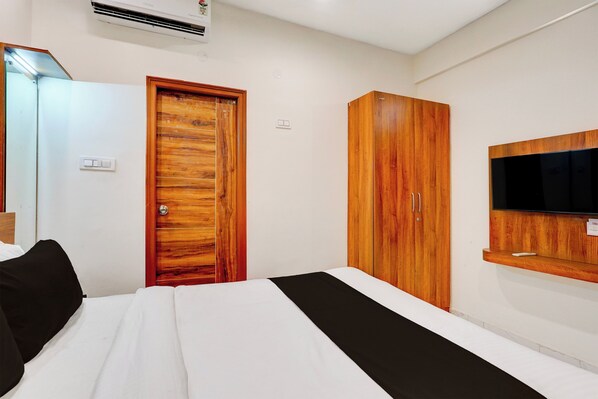 Una habitación de hotel con una cama, un armario, un televisor montado en la pared y un equipo de aire acondicionado.