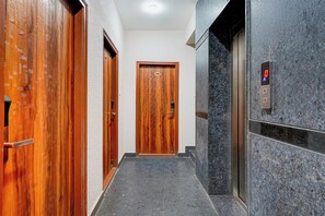 A hallway with wooden doors, a marble wall, and an elevator. - Super Townhouse Marathahalli (Bangalore)