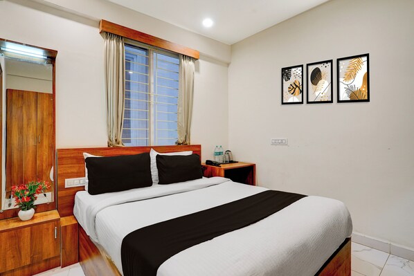 A hotel room with a bed, wooden headboard, a nightstand with a lamp, a mirror, a window with curtains, and three framed artworks on the wall. - Super Townhouse Marathahalli (Bangalore)