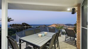 Un espacio comedor al aire libre con techo, vista al mar, una mesa con sillas y una planta en maceta.