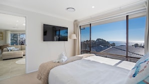 A hotel room with a bed, a TV, a large window with a view of the sea, and a balcony.