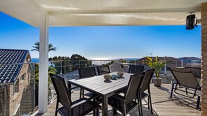 Un patio techado al aire libre con una mesa y sillas, con vista al litoral.