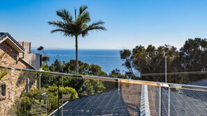 A residential area with a view of the sea, a palm tree, and a building with a sloped roof.
