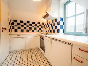 A compact kitchen with a checkered backsplash, white cabinets, and a window with blue trim. - OG in the Reimer House (St. Peter-Ording)
